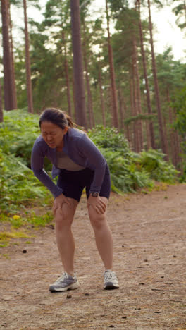 Vertical-Video-Of-Woman-Exercising-Doing-Work-Out-Outdoors-Running-Along-Track-In-Forest-Stopping-For-Breath-Shot-In-Real-Time